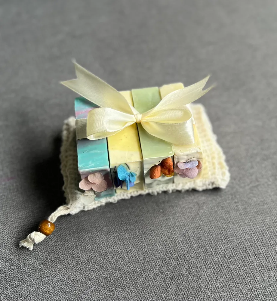 Four botanical soaps tied with ribbon on a soap saver pouch